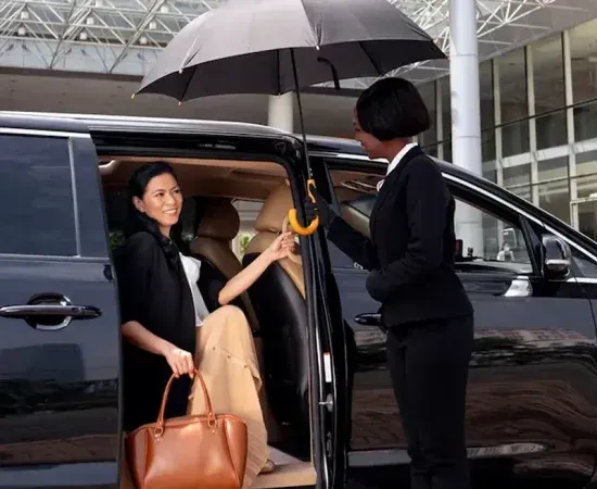 Woman in a suit standing next to a black sedan in front of a modern building